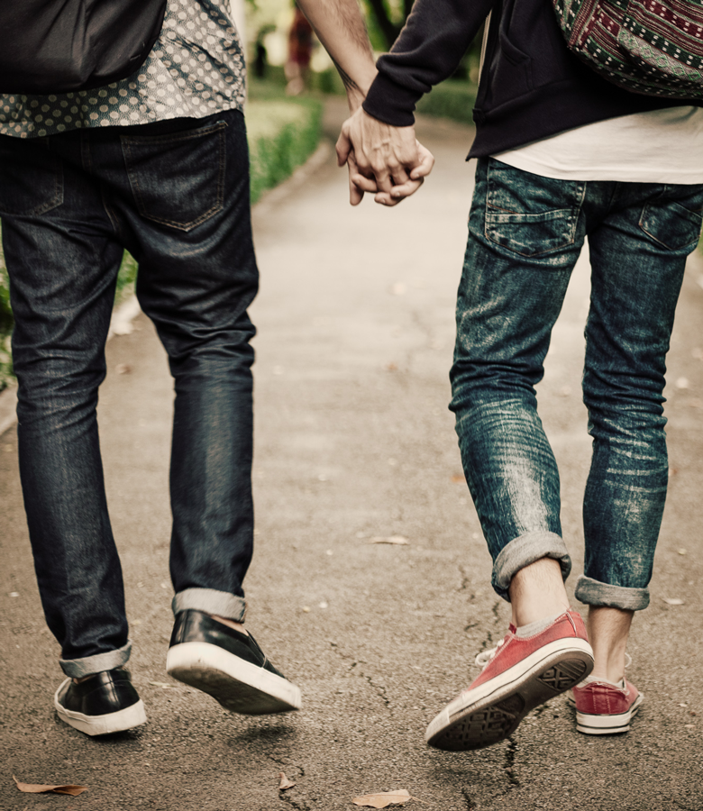 Cropped image of two people holding hands, they are wearing blue denim jeans with converse sneakers. .