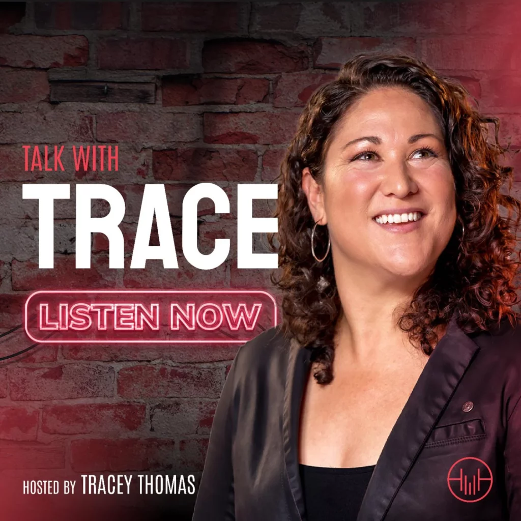Podcast cover "Talk with Trace" shows Tracey Thomas standing in front of a brick wall. Tracey has brown hair, light skin and is wearing a black suit jacket.